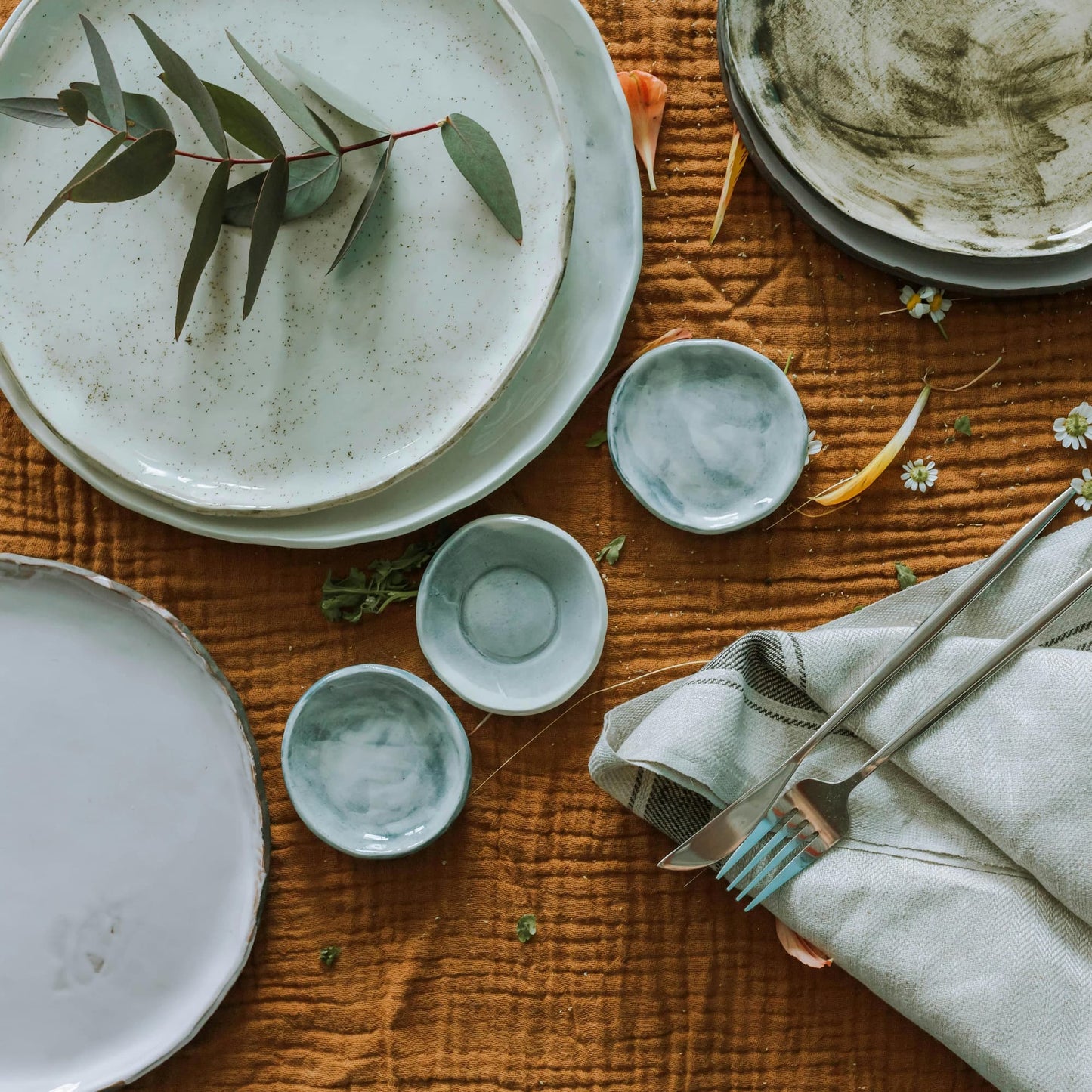 A stack of turquoise plates and bowls artfully arranged with foliage against a red tablecloth.