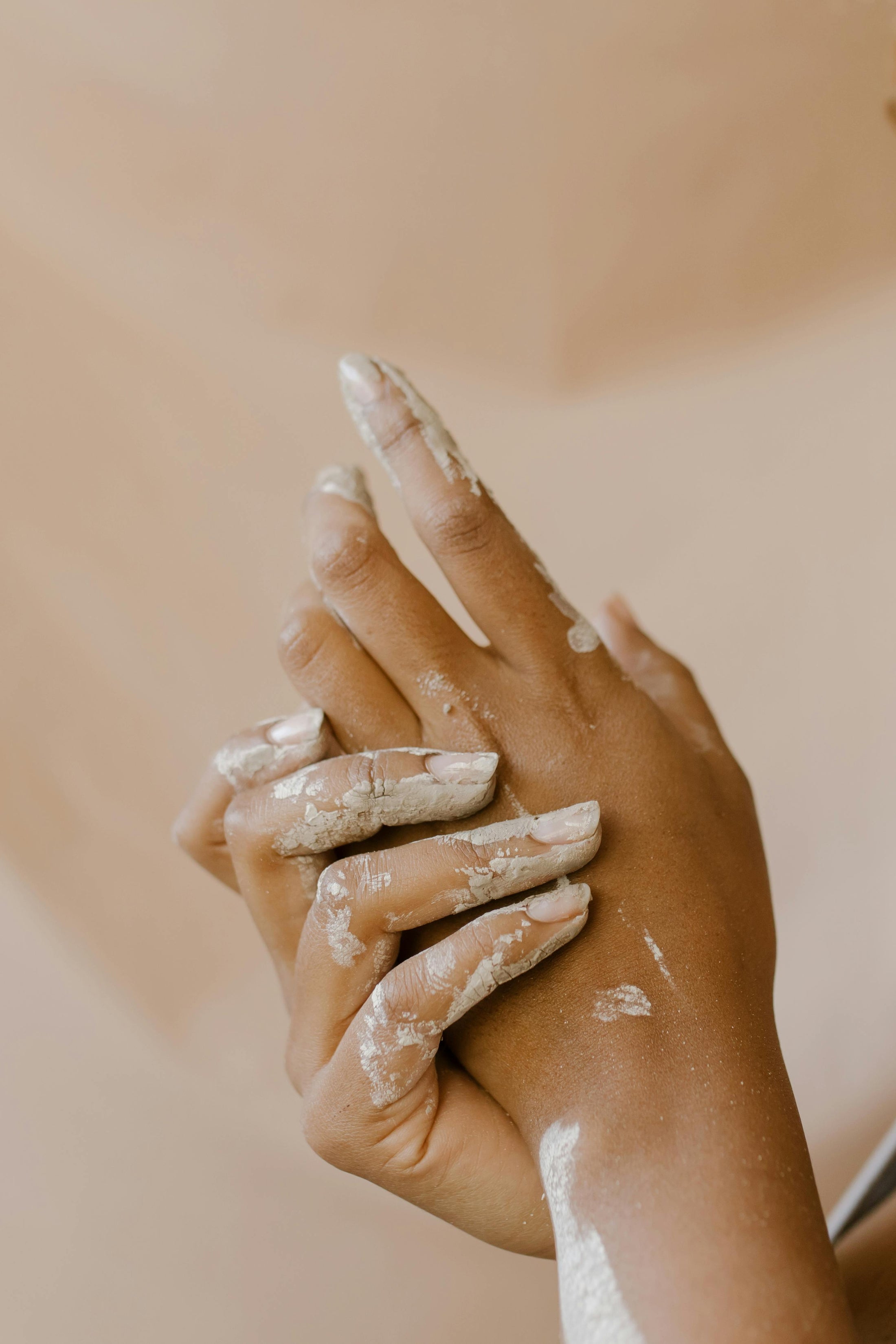 A pair of softly clasped hands, covered in clay.