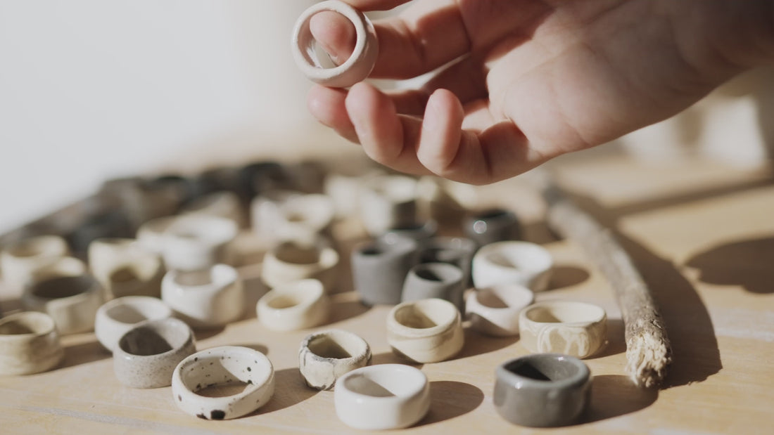 A hand carefully picks up a single ceramic ring out of dozens of unique rings and puts it back down. 